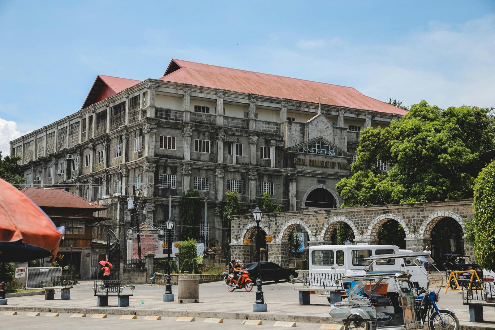 A classic college building surrounded by vibrant urban life and trees.