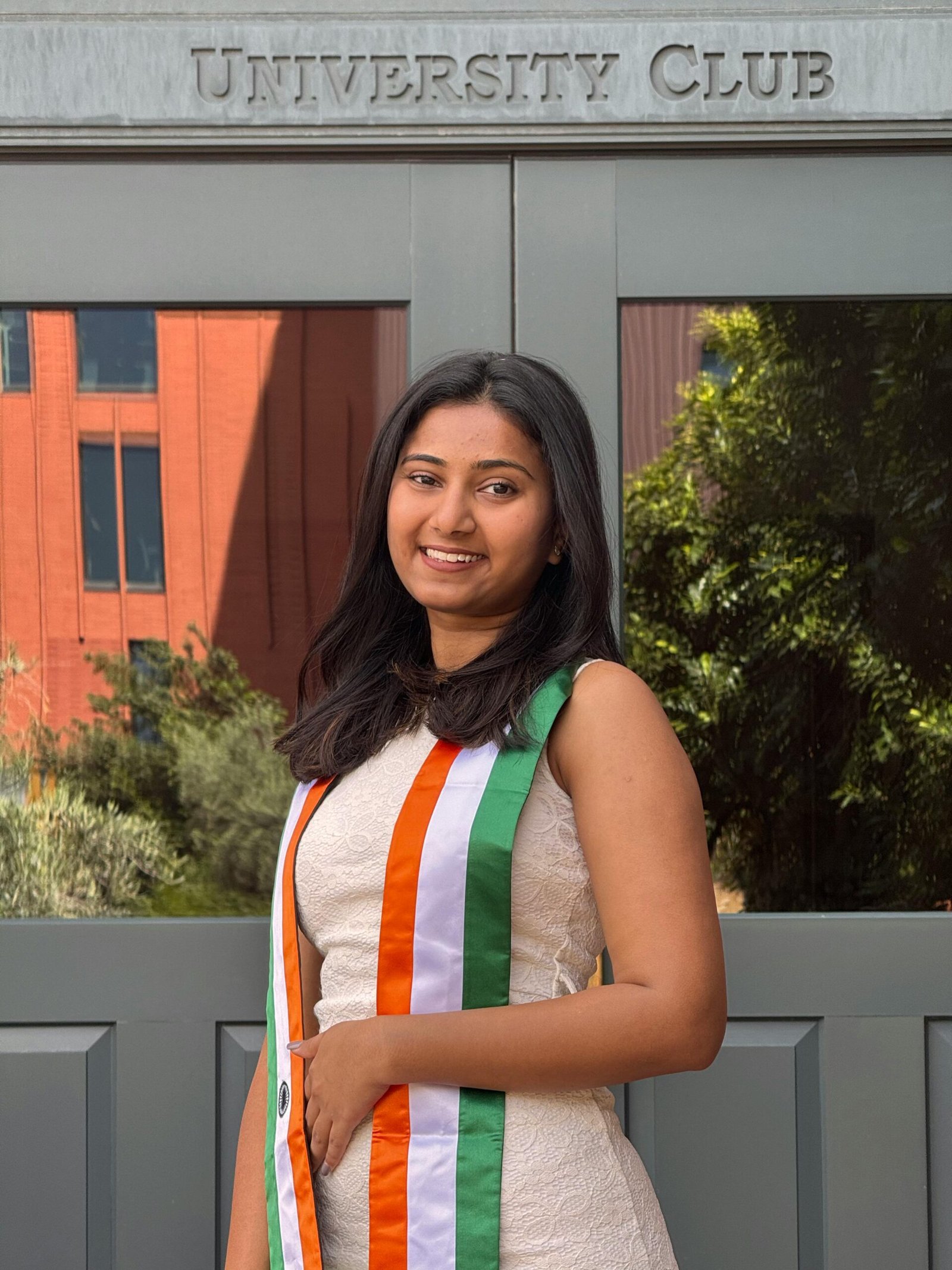 Young woman smiling in front of University Club entrance wearing tricolor sash.