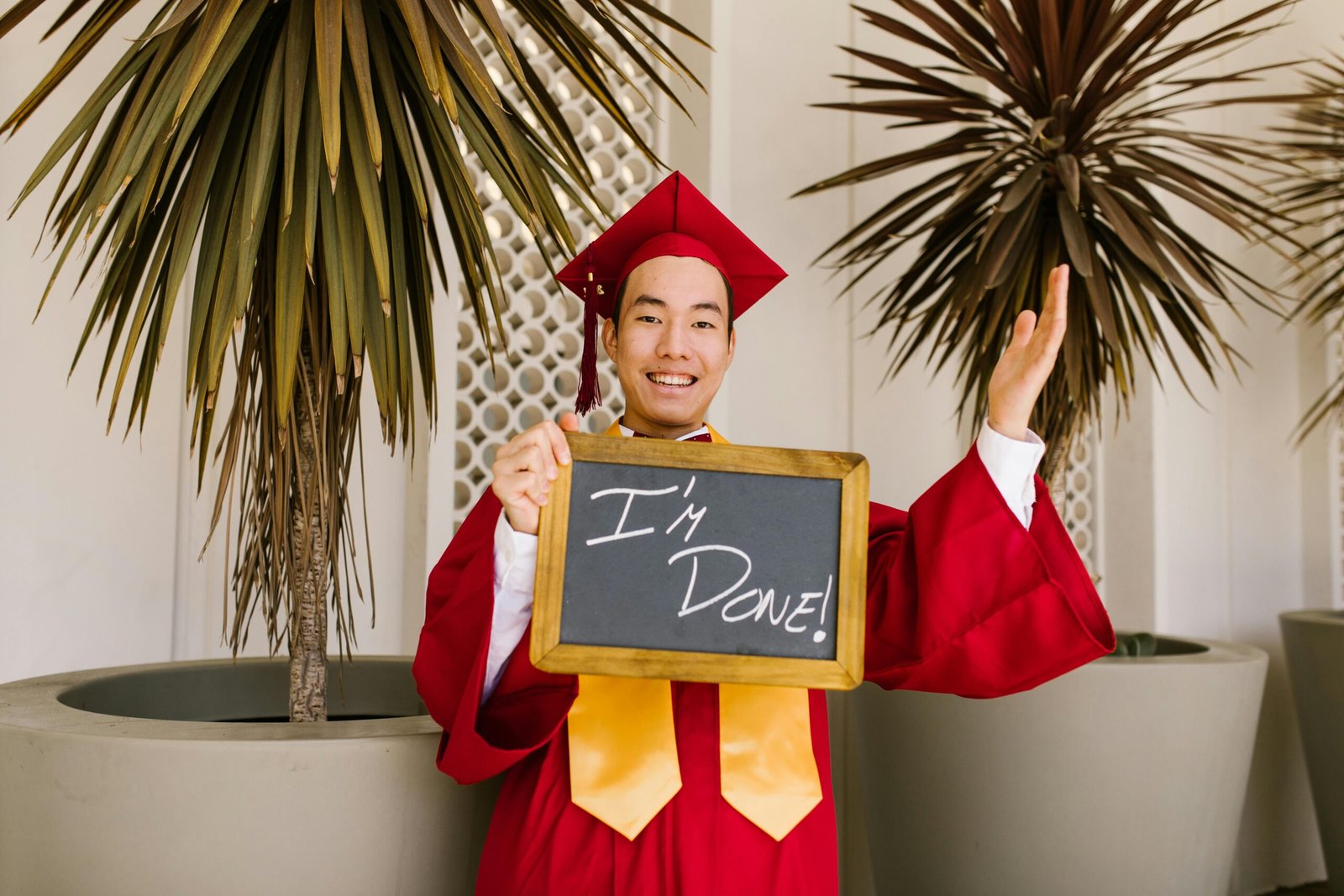 Smiling graduate in red gown holding chalkboard that reads 